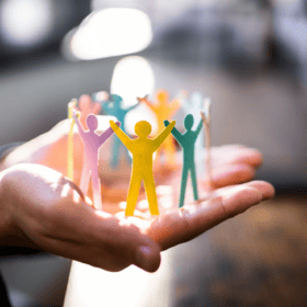 Hand hält bunte Papierfiguren, symbolisieren Teamgeist und Arbeitgeberattraktivität.