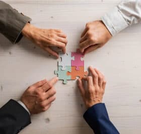 Zwei Hände verbinden Puzzlestücke, symbolisiert Teamarbeit im Gesundheitswesen.
